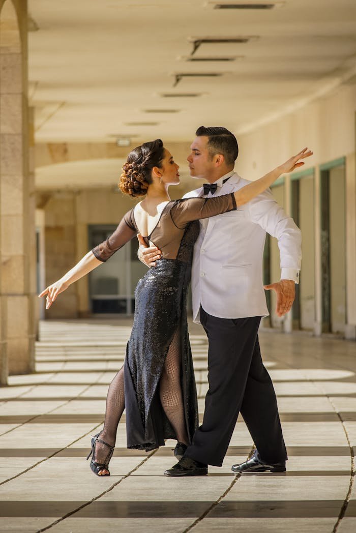 Graceful couple performing ballroom dance in an elegant sunlit corridor.